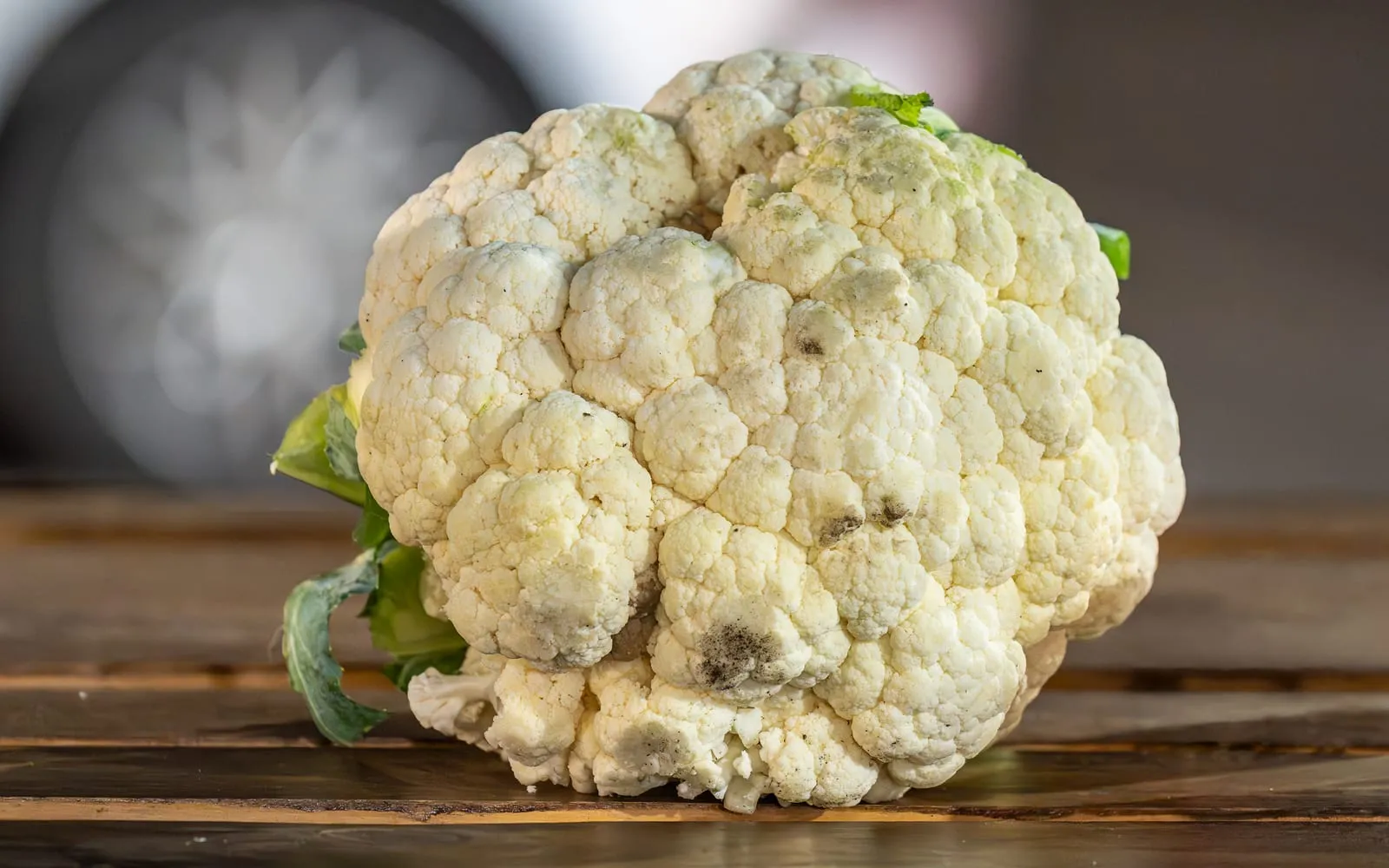 A cauliflower showing its dense white curd with a few green leaves still attached