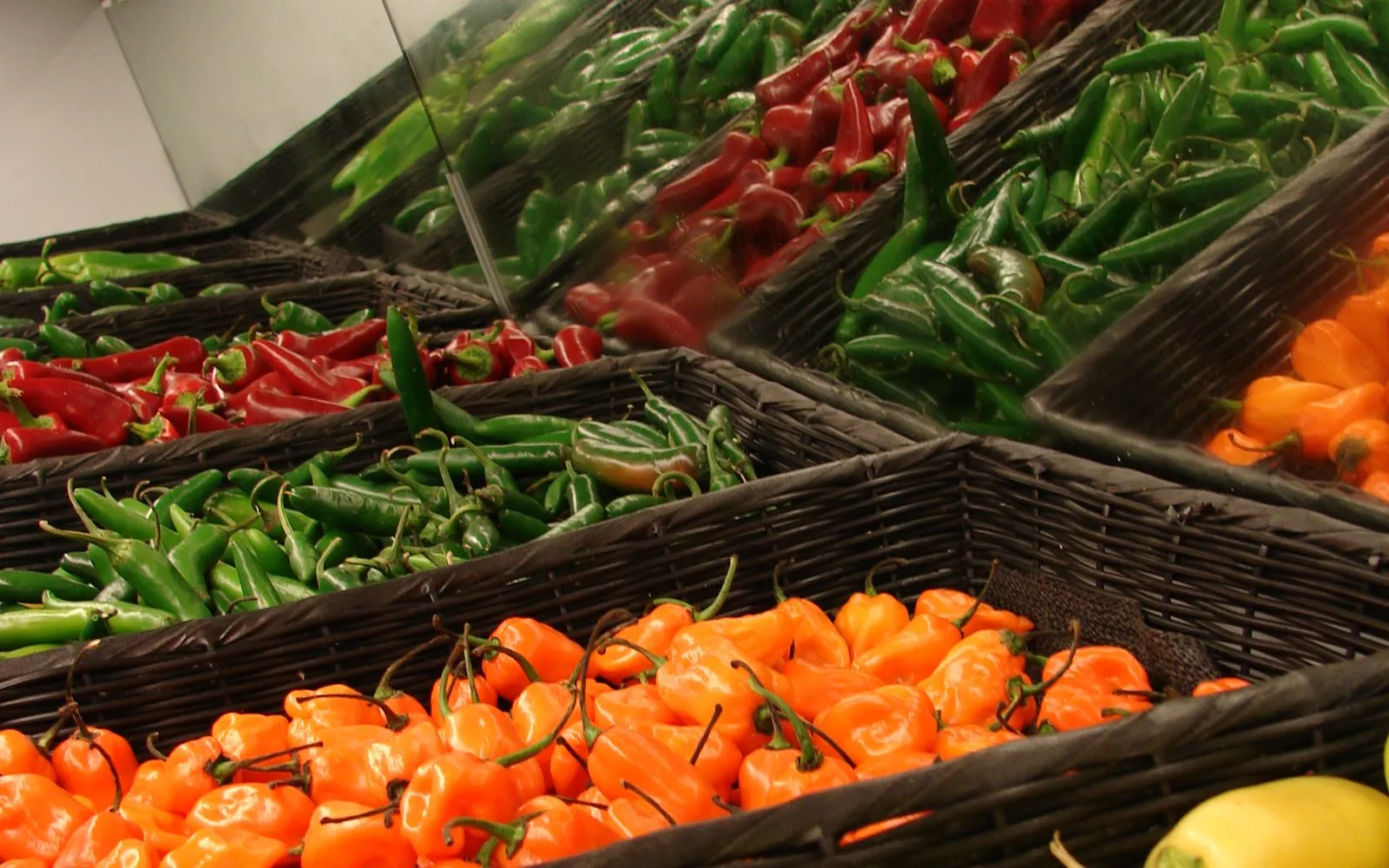 Baskets of chillies at a market stall, sorted by colour into rows of red, green and bright orange habanero-shaped fruit