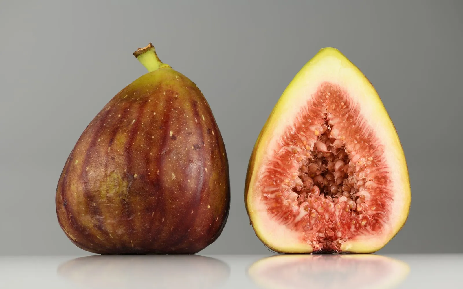 A ripe purple fig beside a second cut in half, showing the pink seeded flesh inside