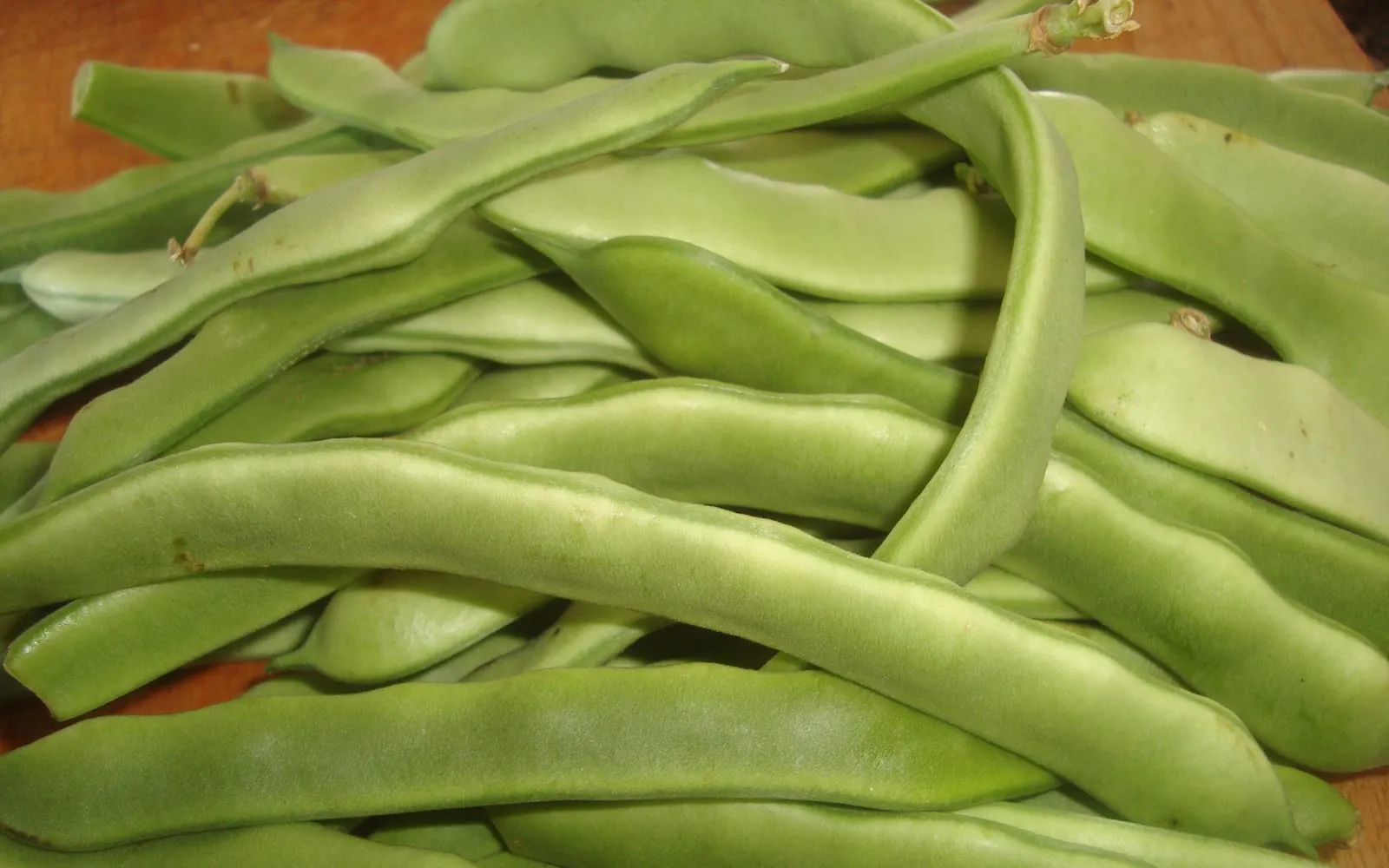 A heap of freshly picked flat green French bean pods on a wooden board