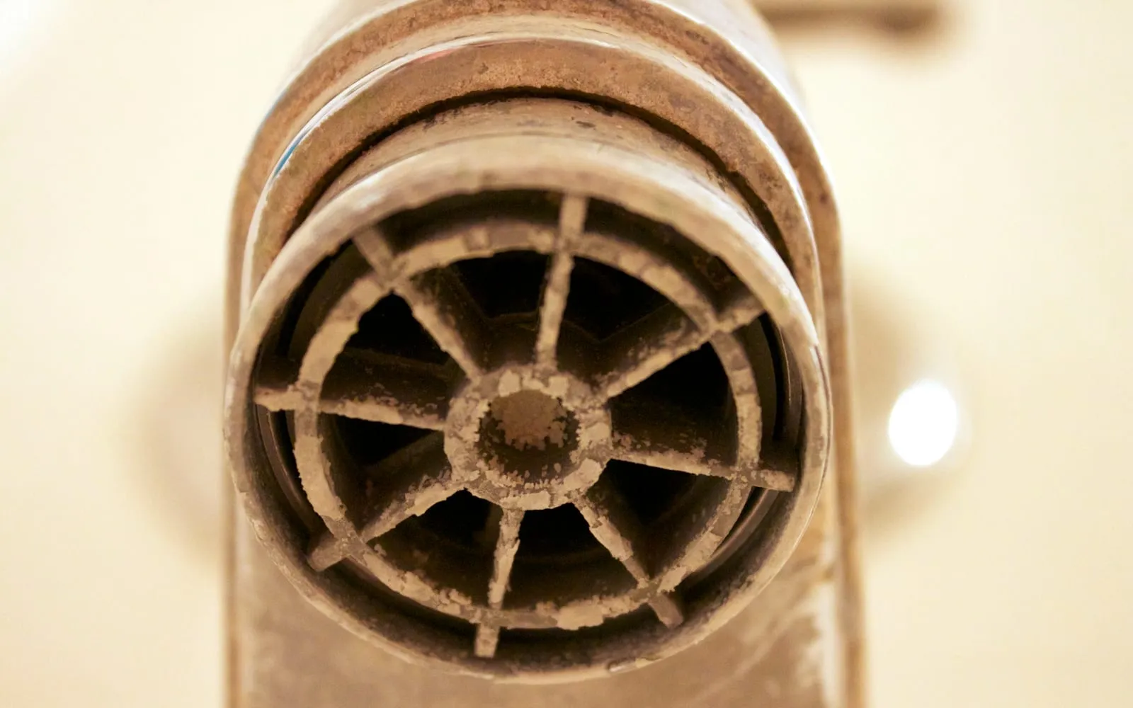 Close-up of a tap spout whose grille and rim are thickly encrusted with buff-white mineral deposit, almost blocking the outlet