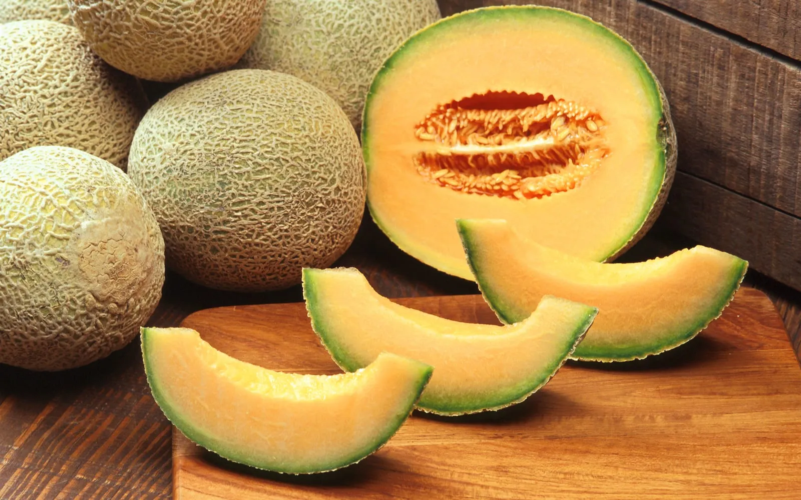 Netted cantaloupe melons whole and cut on a board, showing dense orange flesh around the seed cavity