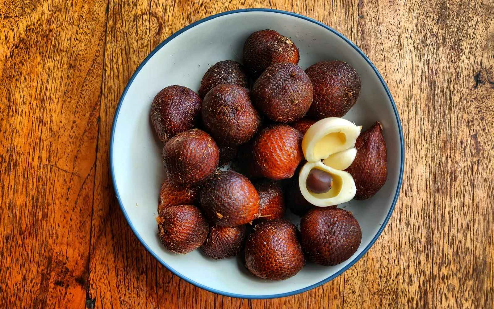 A bowl of scaly red-brown salak, one peeled to show the creamy segments inside